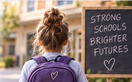Student outside a school beside a Strong Schools Brighter Futures chalkboard